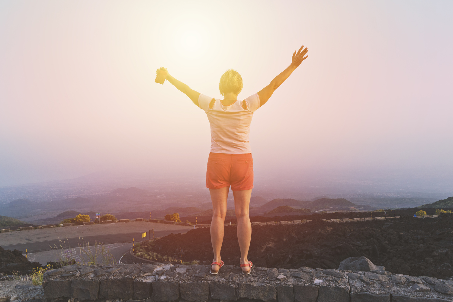 Happy middle-aged woman with raised hands enjoying sunset